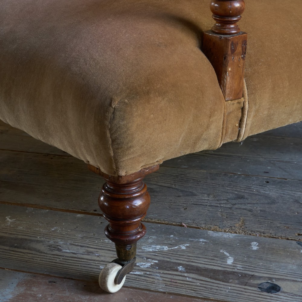 An antique open armchair upholstered in golden brown velvet featuring button-tufting, turned wooden front legs, and castors. View VI