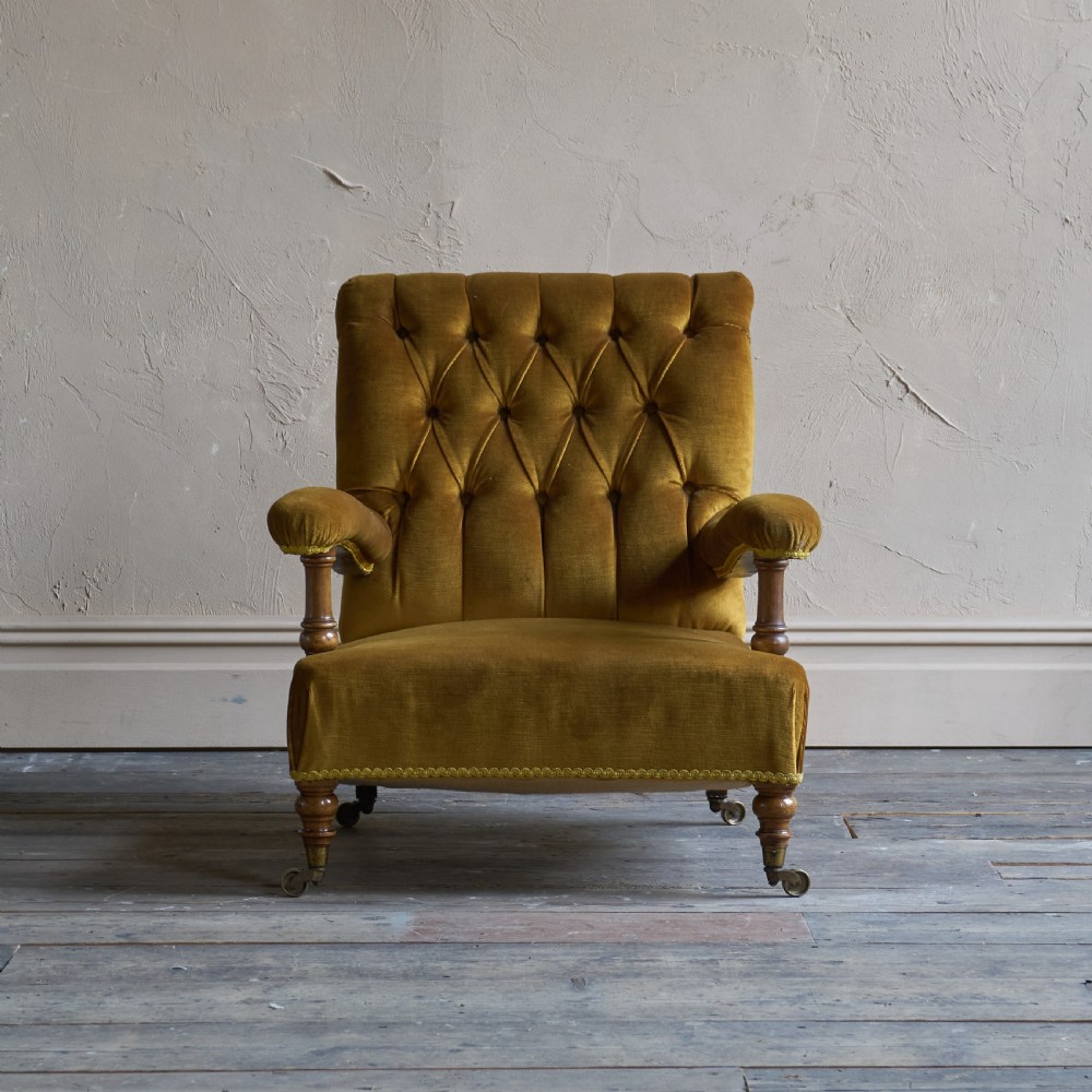An antique open armchair upholstered in gold velvet featuring a button-backed scroll backrest, padded armrests on turned wooden supports, and turned front legs with brass castors. View II