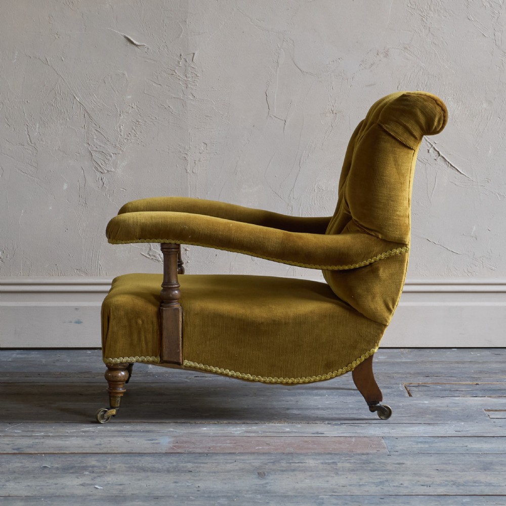 An antique open armchair upholstered in gold velvet featuring a button-backed scroll backrest, padded armrests on turned wooden supports, and turned front legs with brass castors. View III