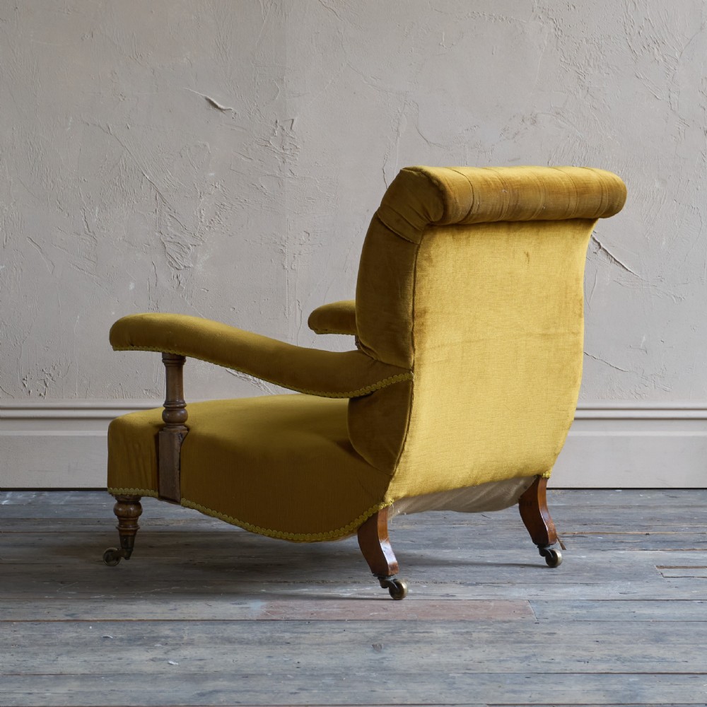An antique open armchair upholstered in gold velvet featuring a button-backed scroll backrest, padded armrests on turned wooden supports, and turned front legs with brass castors. View IV