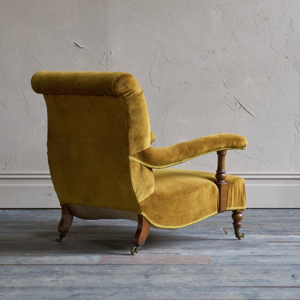 An antique open armchair upholstered in gold velvet featuring a button-backed scroll backrest, padded armrests on turned wooden supports, and turned front legs with brass castors. View V