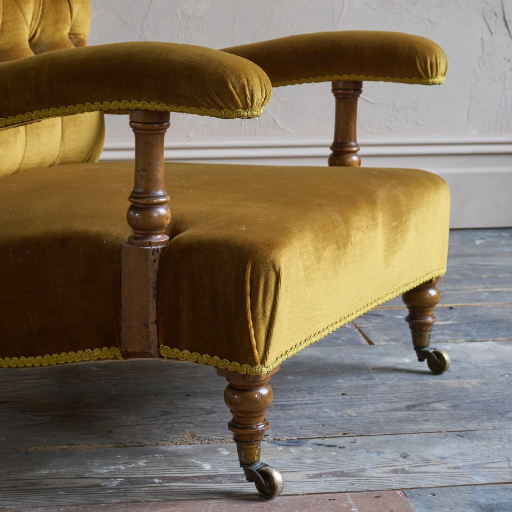 An antique open armchair upholstered in gold velvet featuring a button-backed scroll backrest, padded armrests on turned wooden supports, and turned front legs with brass castors. View VII