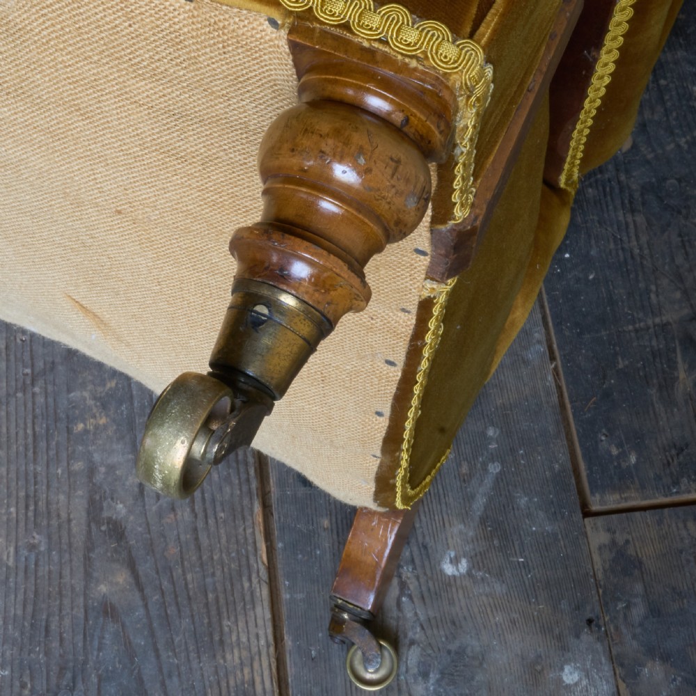 An antique open armchair upholstered in gold velvet featuring a button-backed scroll backrest, padded armrests on turned wooden supports, and turned front legs with brass castors. View VIII