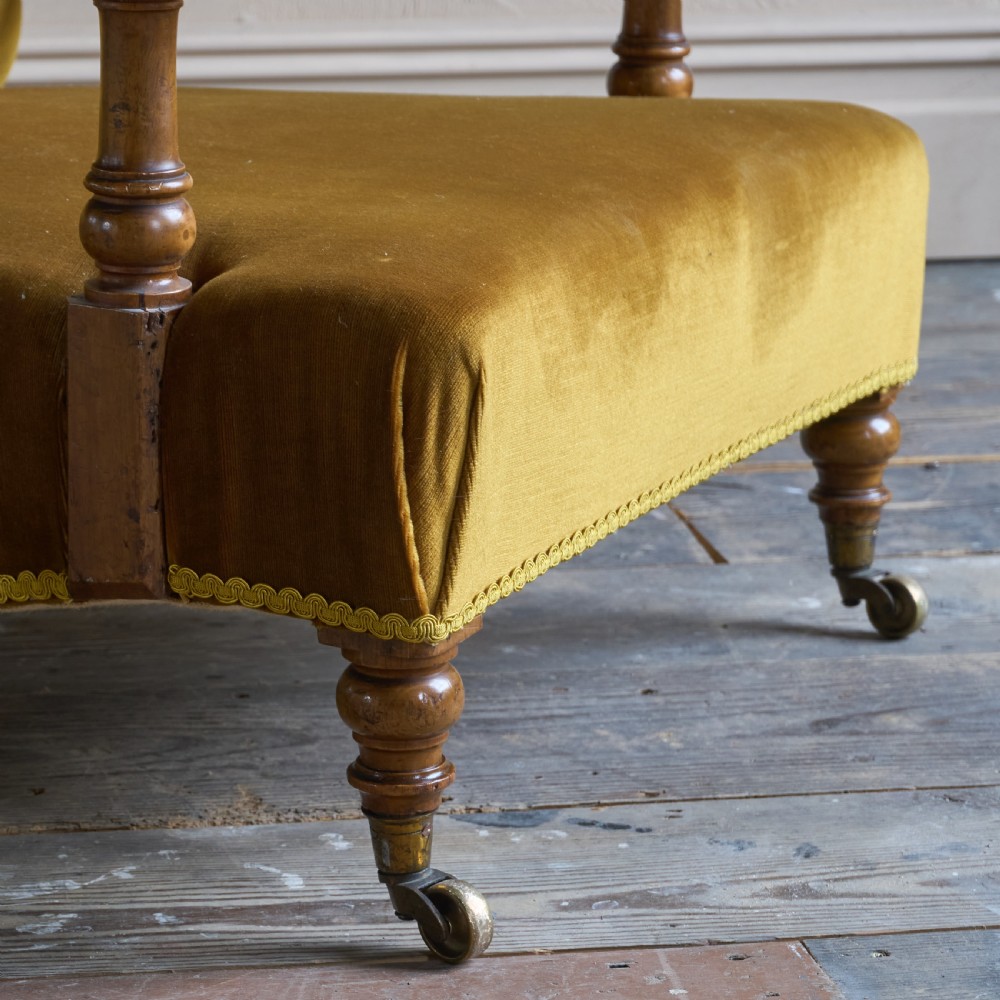 An antique open armchair upholstered in gold velvet featuring a button-backed scroll backrest, padded armrests on turned wooden supports, and turned front legs with brass castors. View IX