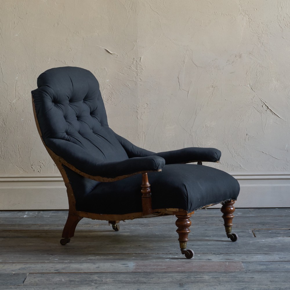 A Victorian open armchair upholstered in black calico, featuring a button-tufted inclined backrest, turned wooden arm uprights, and turned front legs fitted with brass castors.