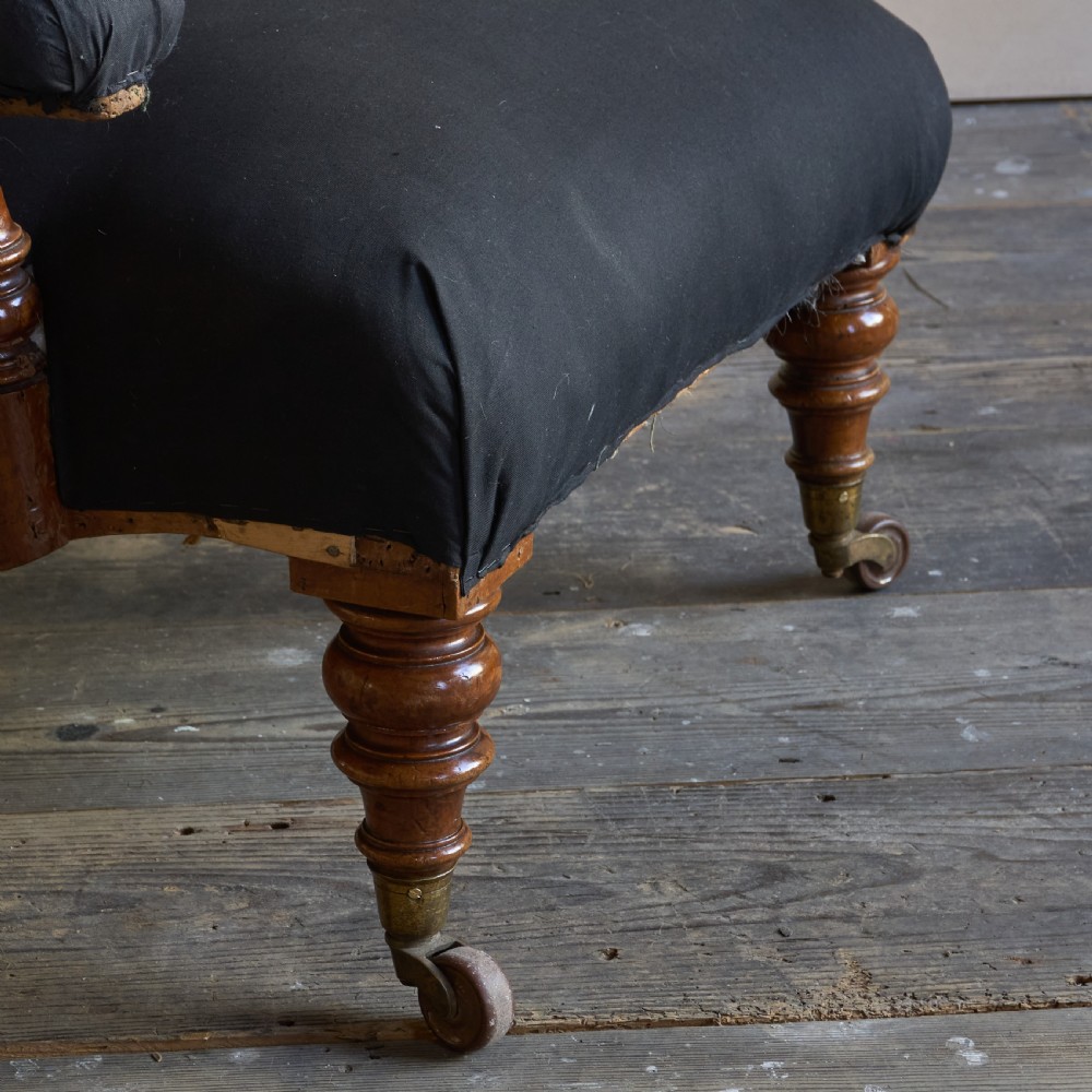 A Victorian open armchair upholstered in black calico, featuring a button-tufted inclined backrest, turned wooden arm uprights, and turned front legs fitted with brass castors. View II