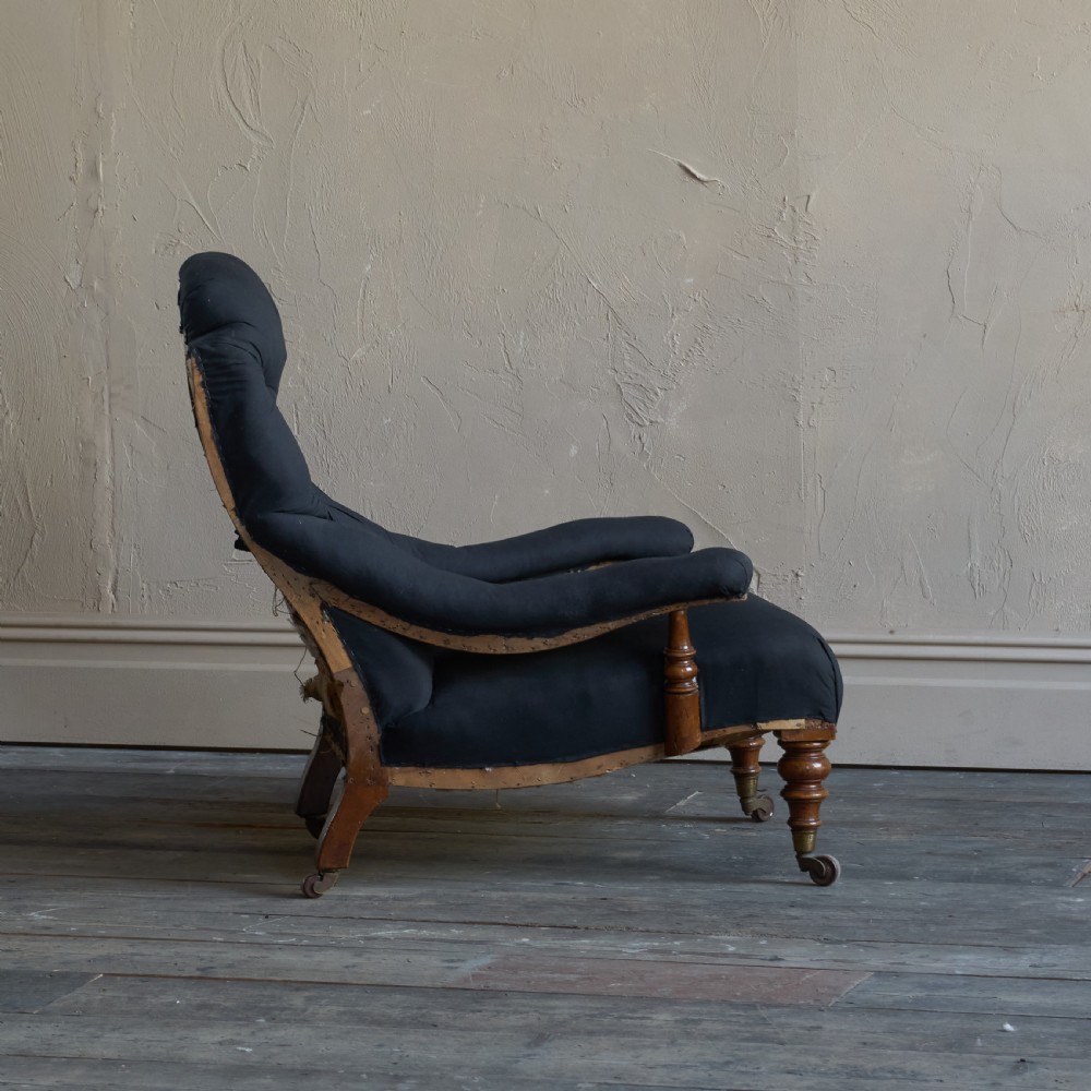 A Victorian open armchair upholstered in black calico, featuring a button-tufted inclined backrest, turned wooden arm uprights, and turned front legs fitted with brass castors. View IV