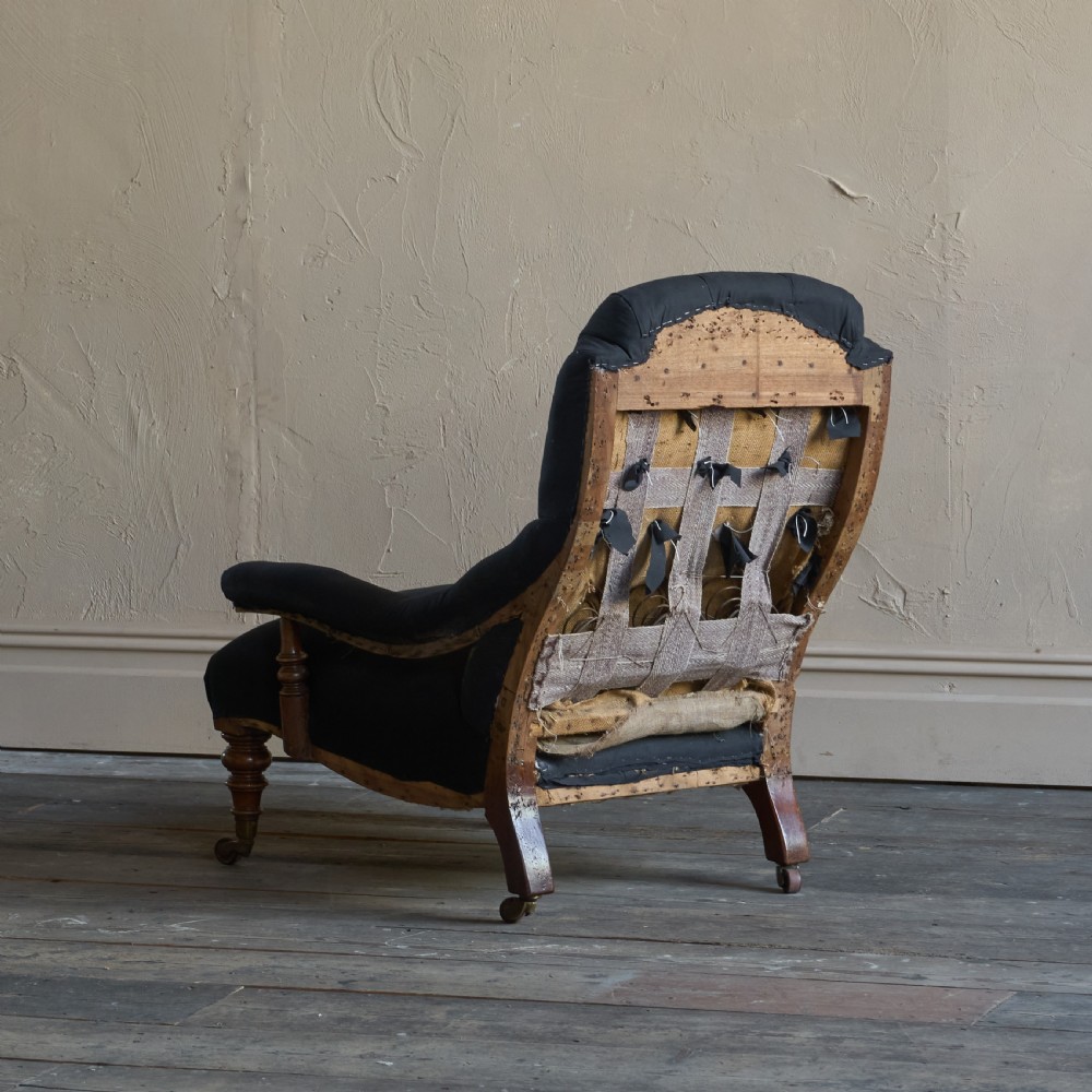 A Victorian open armchair upholstered in black calico, featuring a button-tufted inclined backrest, turned wooden arm uprights, and turned front legs fitted with brass castors. View V