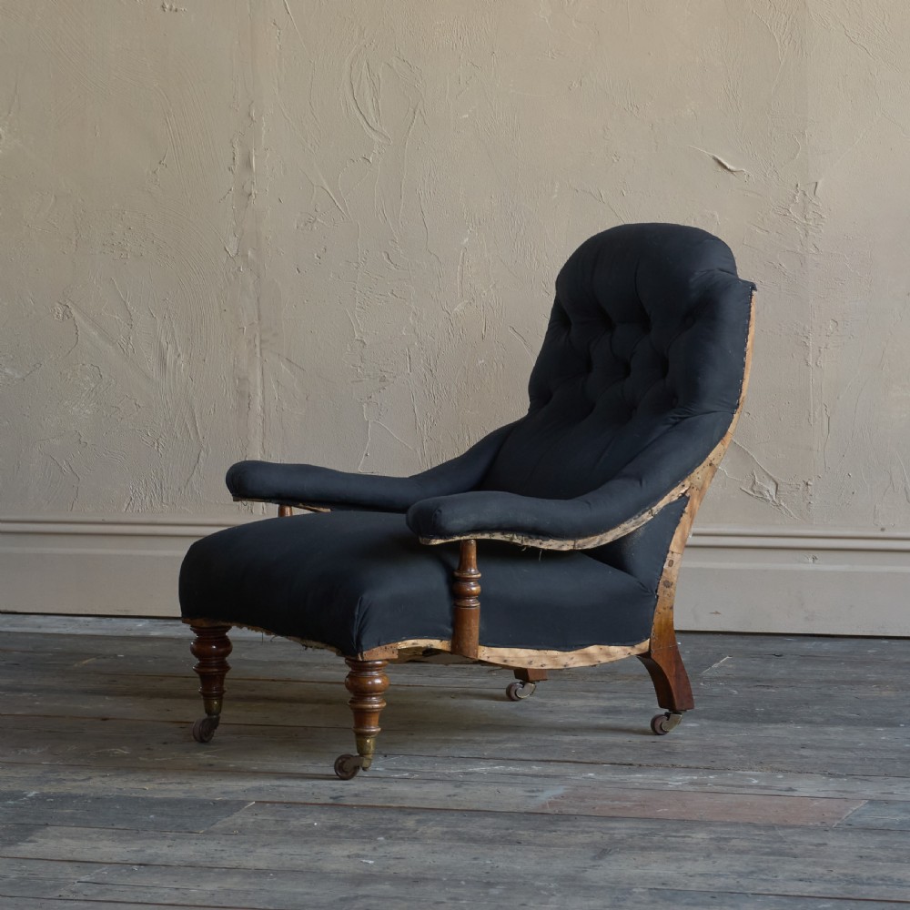 A Victorian open armchair upholstered in black calico, featuring a button-tufted inclined backrest, turned wooden arm uprights, and turned front legs fitted with brass castors. View VI