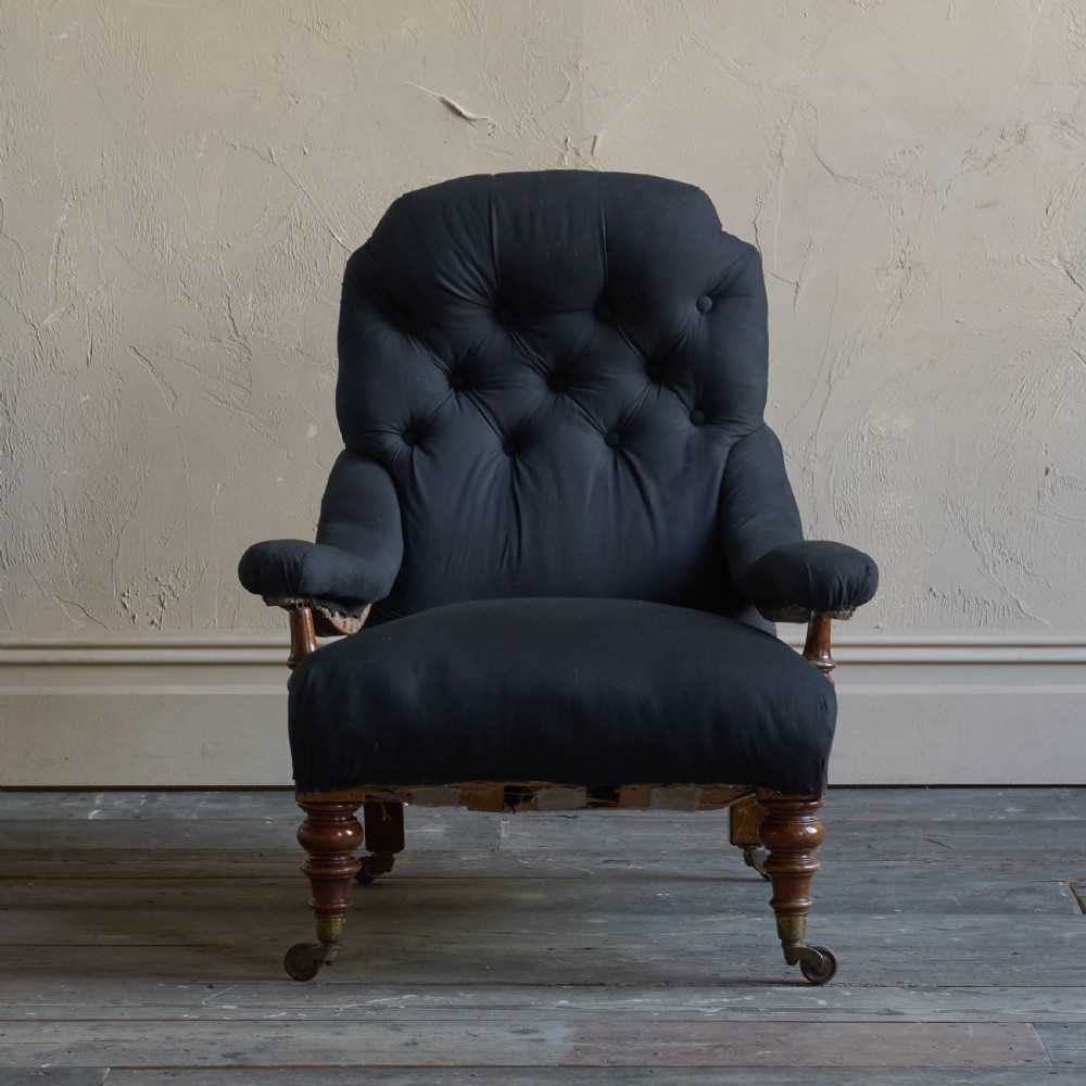 A Victorian open armchair upholstered in black calico, featuring a button-tufted inclined backrest, turned wooden arm uprights, and turned front legs fitted with brass castors. View VII