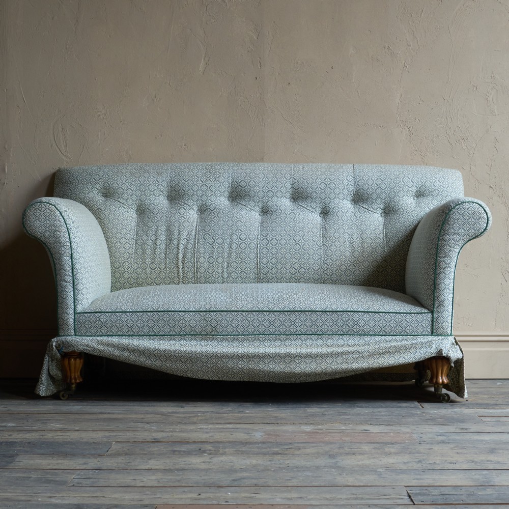 A Regency style upholstered library sofa with button-backed backrest, scrolled arms, pale green patterned fabric with dark piping, and turned legs on brass castors.