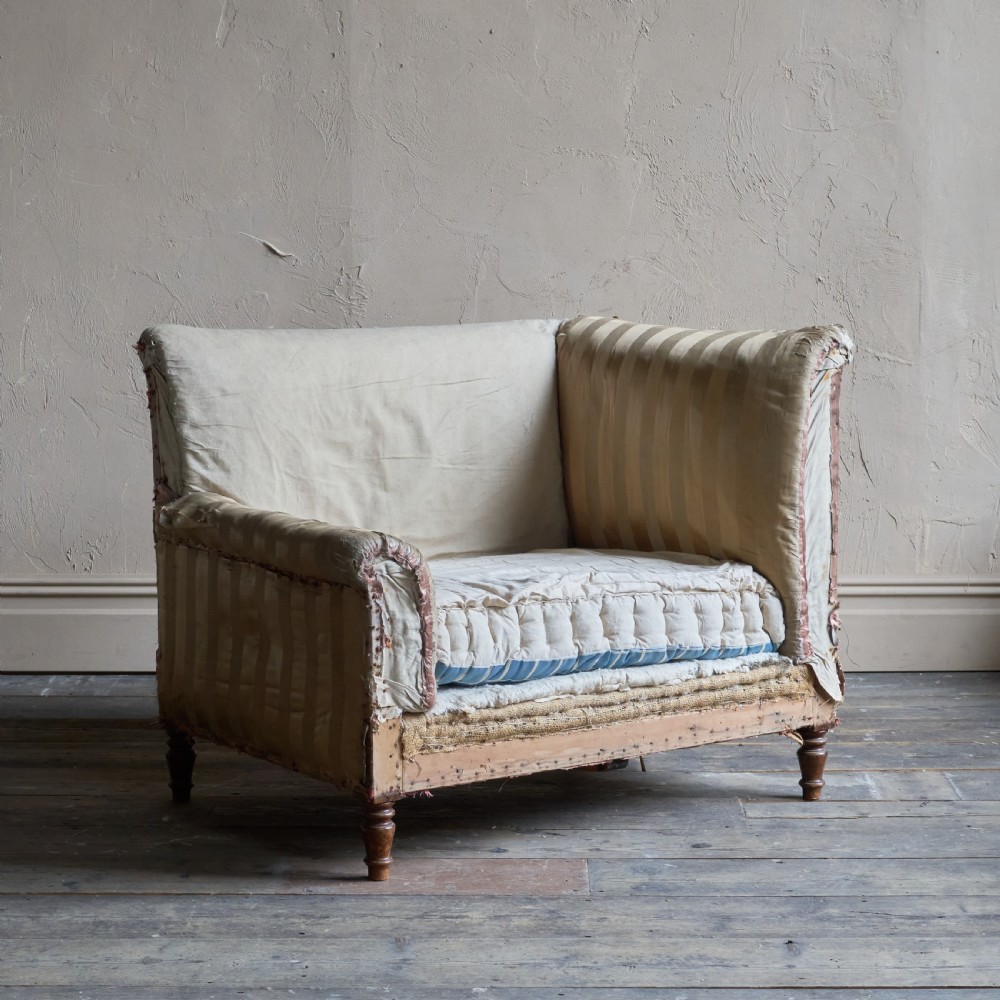 An antique upholstered corner armchair featuring turned wooden legs, striped satin fabric, and a thick tufted squab cushion.