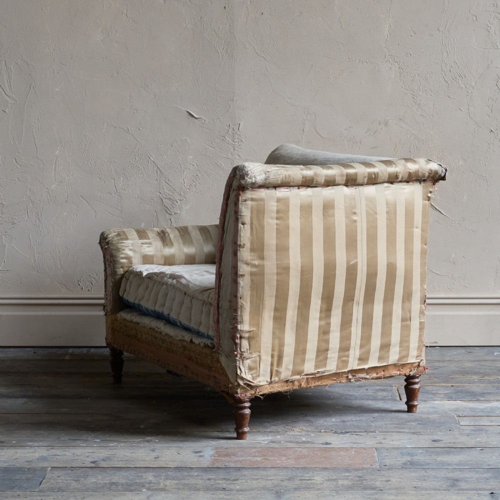 An antique upholstered corner armchair featuring turned wooden legs, striped satin fabric, and a thick tufted squab cushion. View III