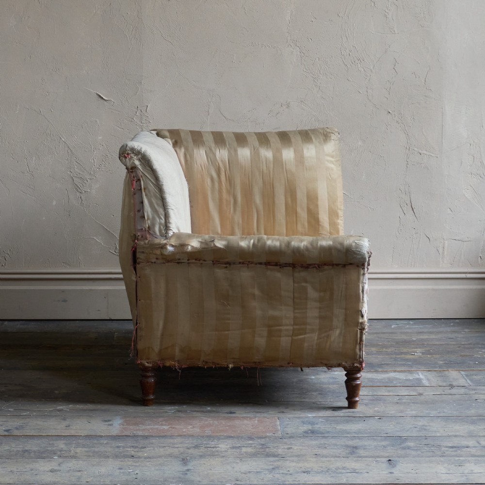 An antique upholstered corner armchair featuring turned wooden legs, striped satin fabric, and a thick tufted squab cushion. View V