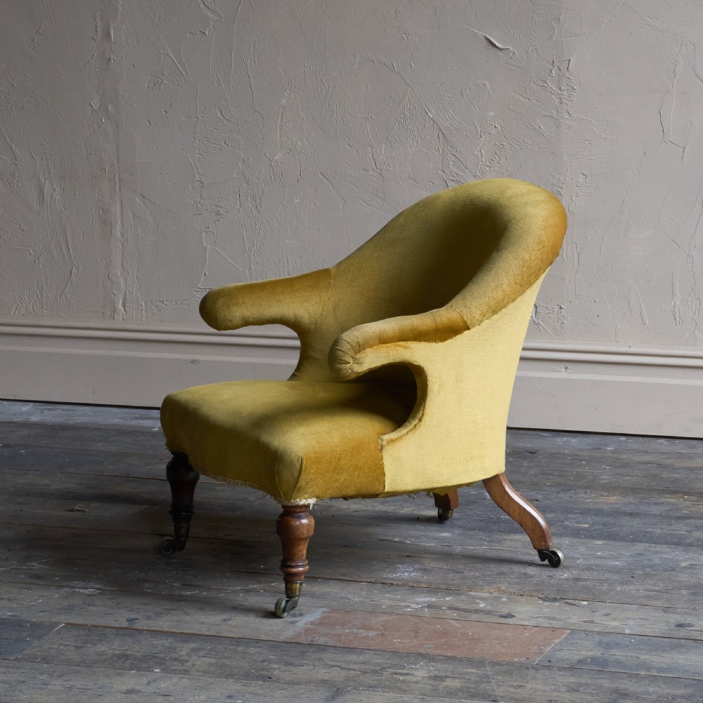 A Victorian low-slung armchair with a curved back, upholstered in mustard yellow velvet, featuring turned front legs with brass castors.