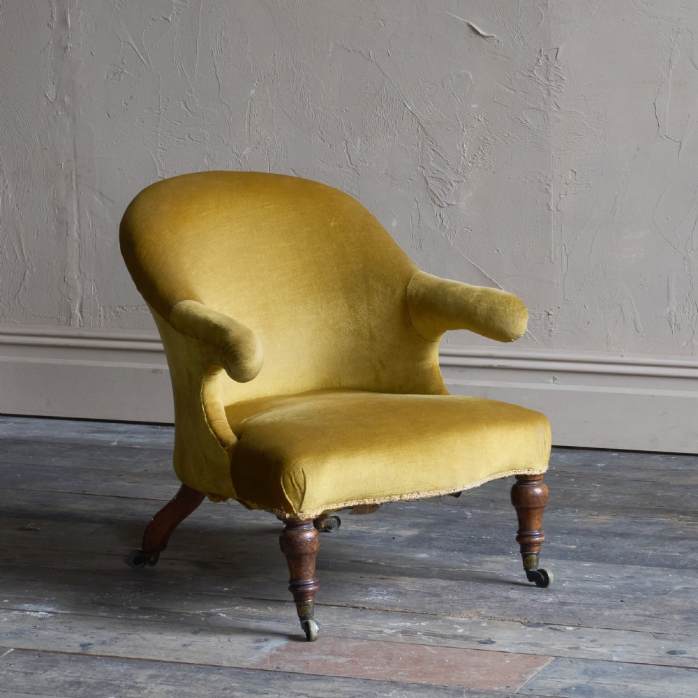 A Victorian low-slung armchair with a curved back, upholstered in mustard yellow velvet, featuring turned front legs with brass castors. View III