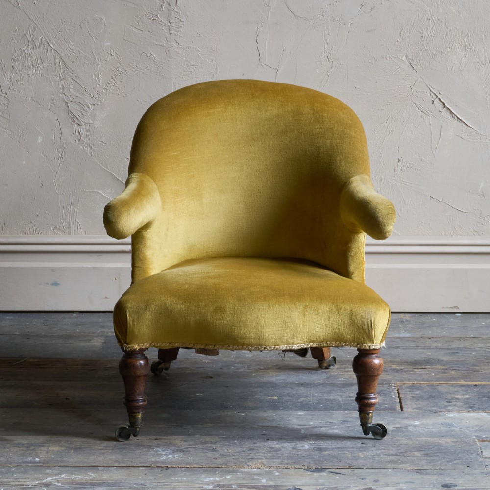 A Victorian low-slung armchair with a curved back, upholstered in mustard yellow velvet, featuring turned front legs with brass castors. View IV