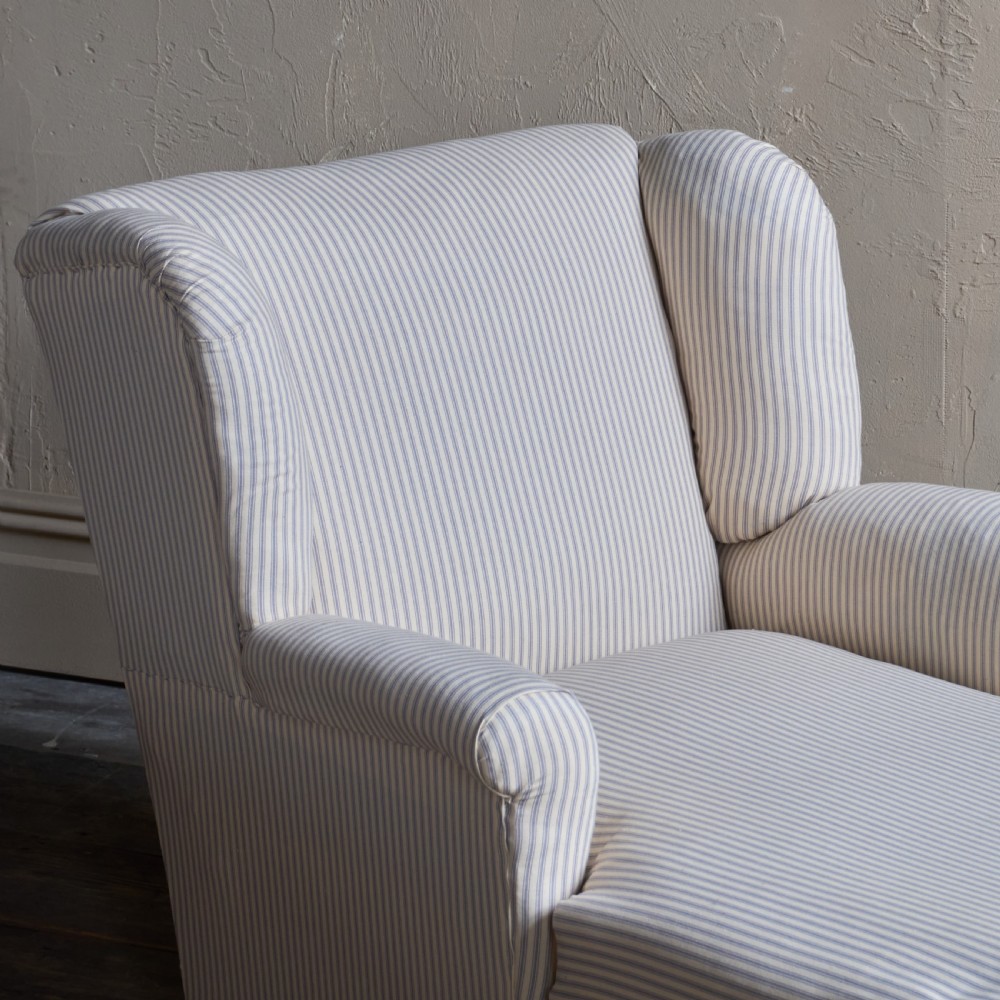 An antique upholstered chaise longue in a cream and beige ticking stripe fabric with a high winged backrest and integrated storage compartment. View II