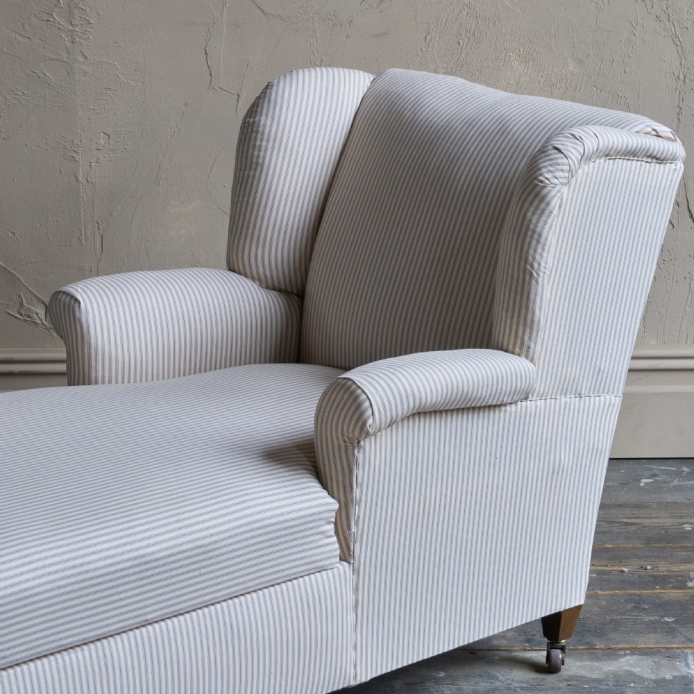 An antique upholstered chaise longue in a cream and beige ticking stripe fabric with a high winged backrest and integrated storage compartment. View III