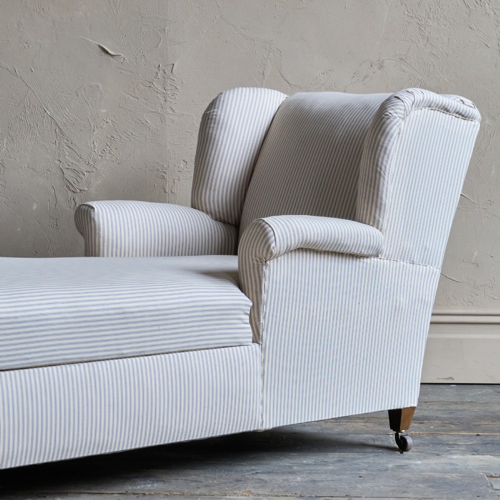 An antique upholstered chaise longue in a cream and beige ticking stripe fabric with a high winged backrest and integrated storage compartment. View V