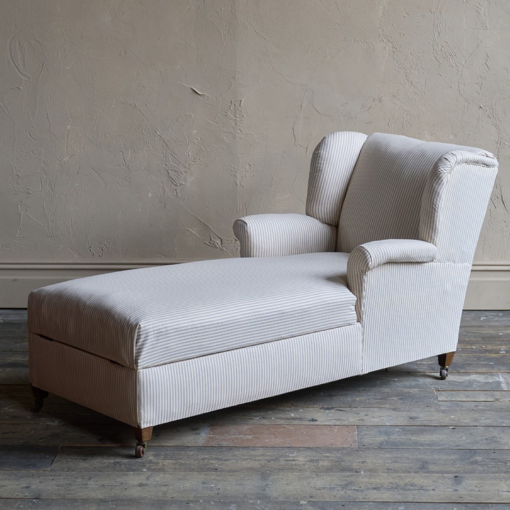 An antique upholstered chaise longue in a cream and beige ticking stripe fabric with a high winged backrest and integrated storage compartment. View VI