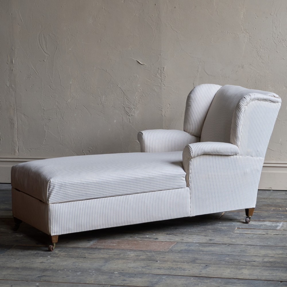 An antique upholstered chaise longue in a cream and beige ticking stripe fabric with a high winged backrest and integrated storage compartment. View VII