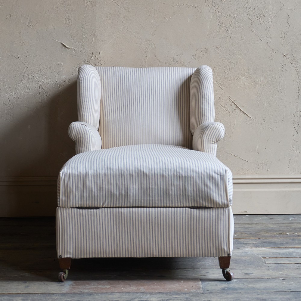 An antique upholstered chaise longue in a cream and beige ticking stripe fabric with a high winged backrest and integrated storage compartment. View VIII