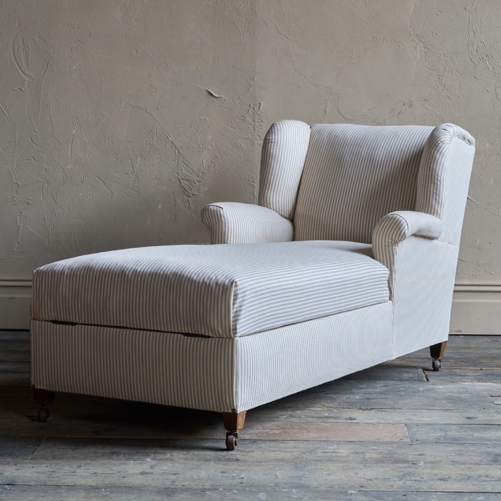 An antique upholstered chaise longue in a cream and beige ticking stripe fabric with a high winged backrest and integrated storage compartment. View IX