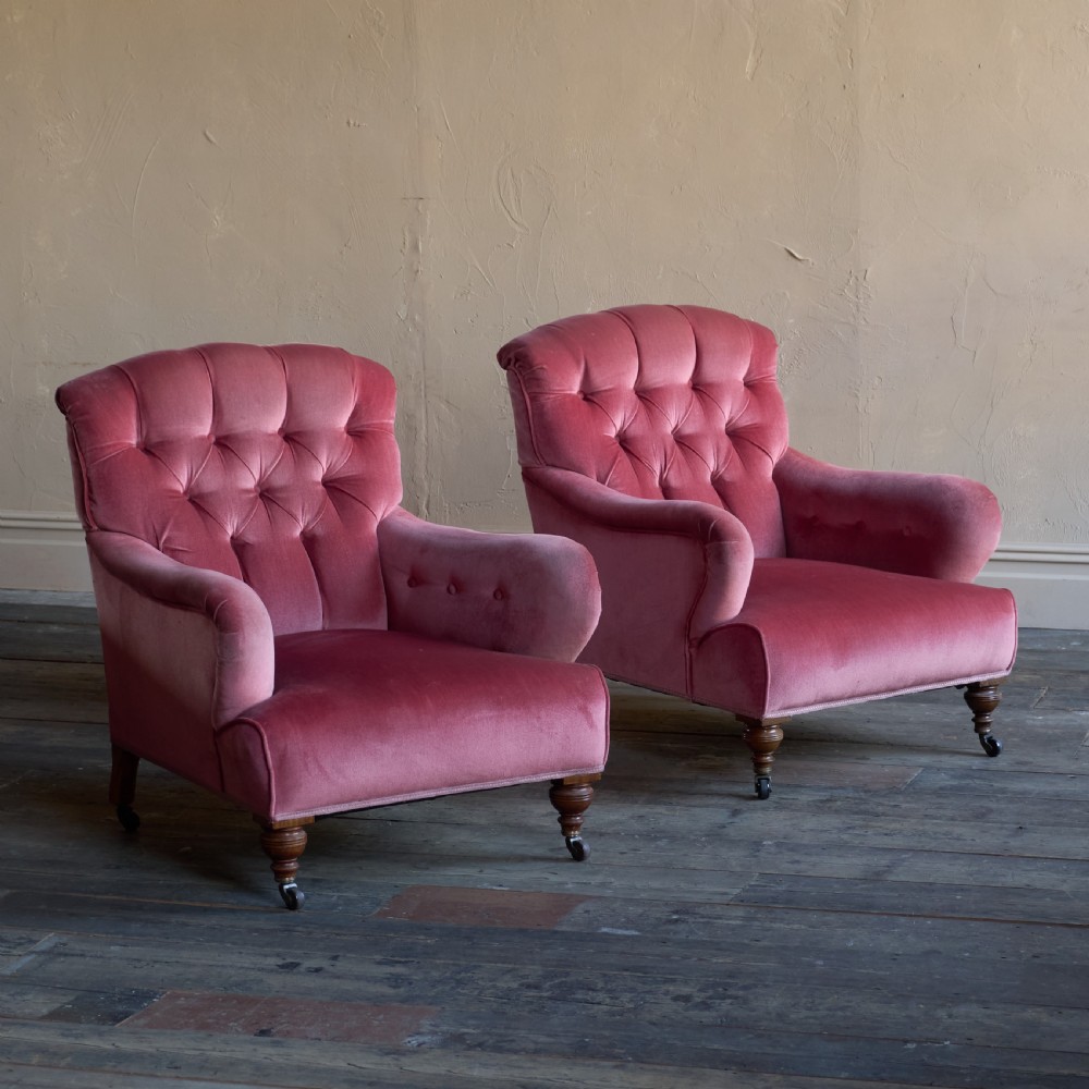 A pair of deep-seated Howard style armchairs upholstered in rose pink velvet featuring button-tufted backrests and turned wooden legs on castors. View II