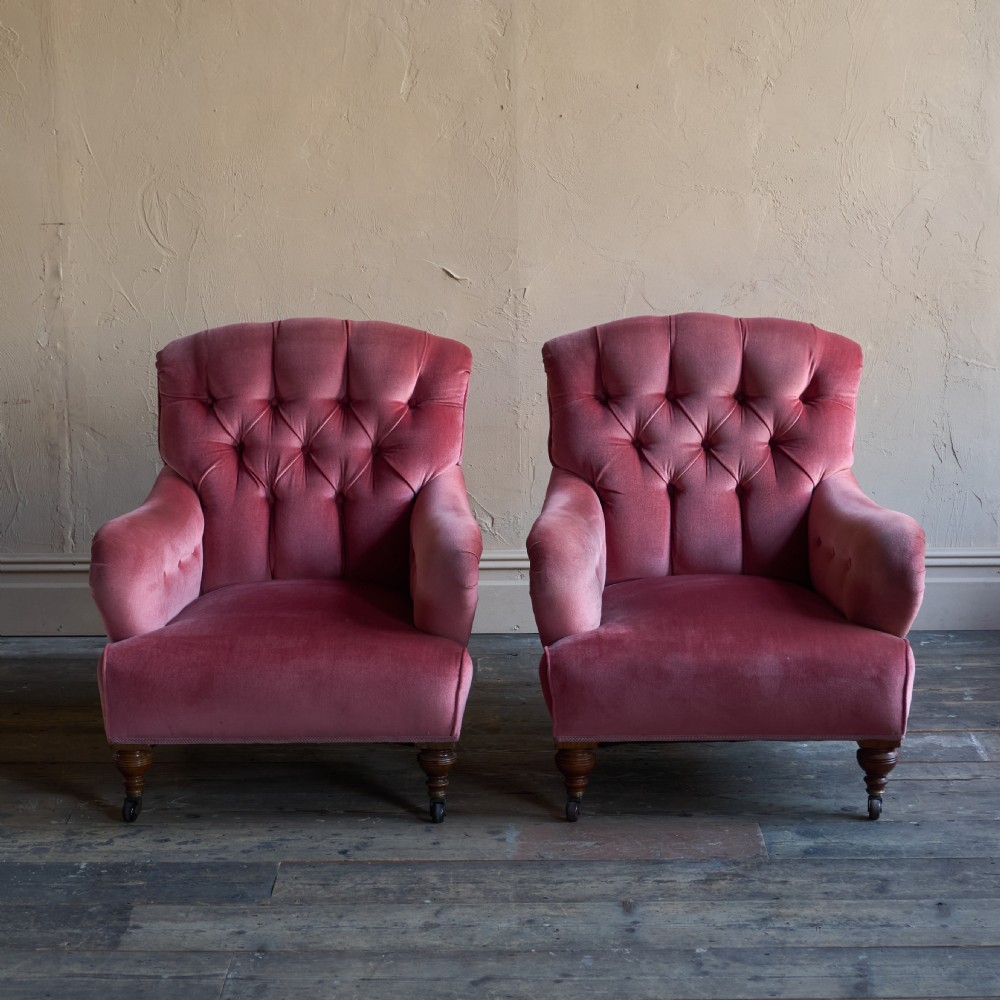 A pair of deep-seated Howard style armchairs upholstered in rose pink velvet featuring button-tufted backrests and turned wooden legs on castors. View III