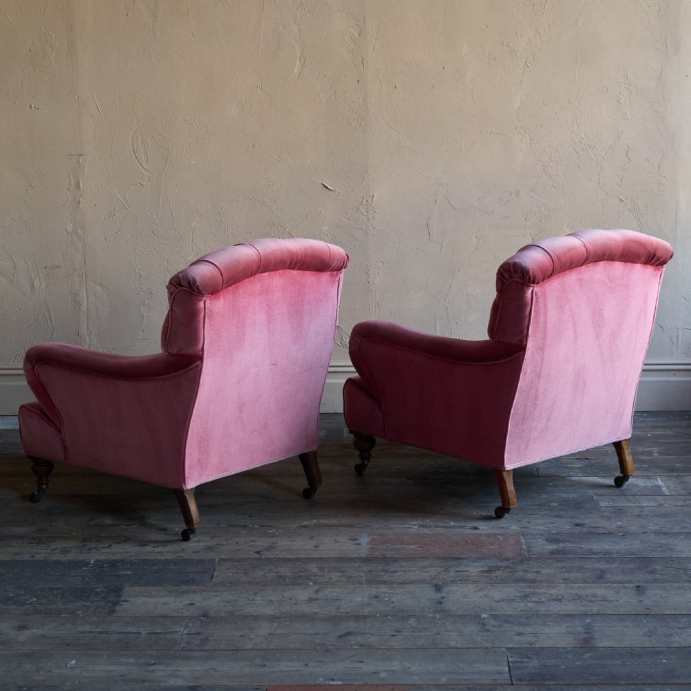 A pair of deep-seated Howard style armchairs upholstered in rose pink velvet featuring button-tufted backrests and turned wooden legs on castors. View V