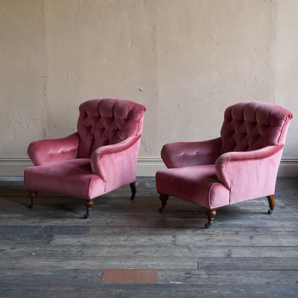 A pair of deep-seated Howard style armchairs upholstered in rose pink velvet featuring button-tufted backrests and turned wooden legs on castors. View VII