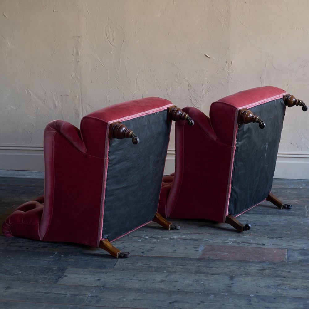A pair of deep-seated Howard style armchairs upholstered in rose pink velvet featuring button-tufted backrests and turned wooden legs on castors. View IX