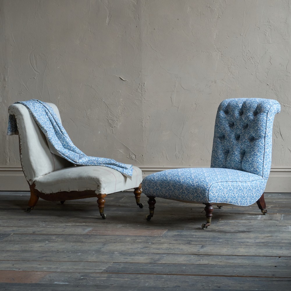 A pair of antique Victorian upholstered armchairs featuring blue and white patterned fabric, tufted backs, and turned wooden legs with brass castors.