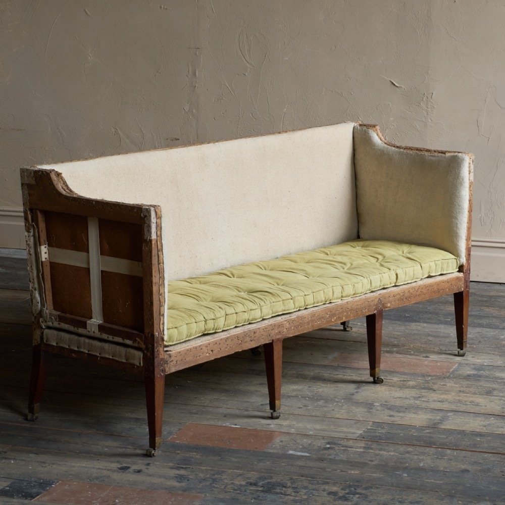An antique Georgian square-back sofa featuring exposed wooden framing, eight legs with castors, and a yellow tufted seat cushion.