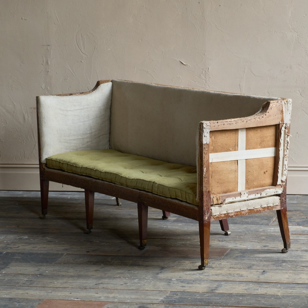 An antique Georgian square-back sofa featuring exposed wooden framing, eight legs with castors, and a yellow tufted seat cushion. View II