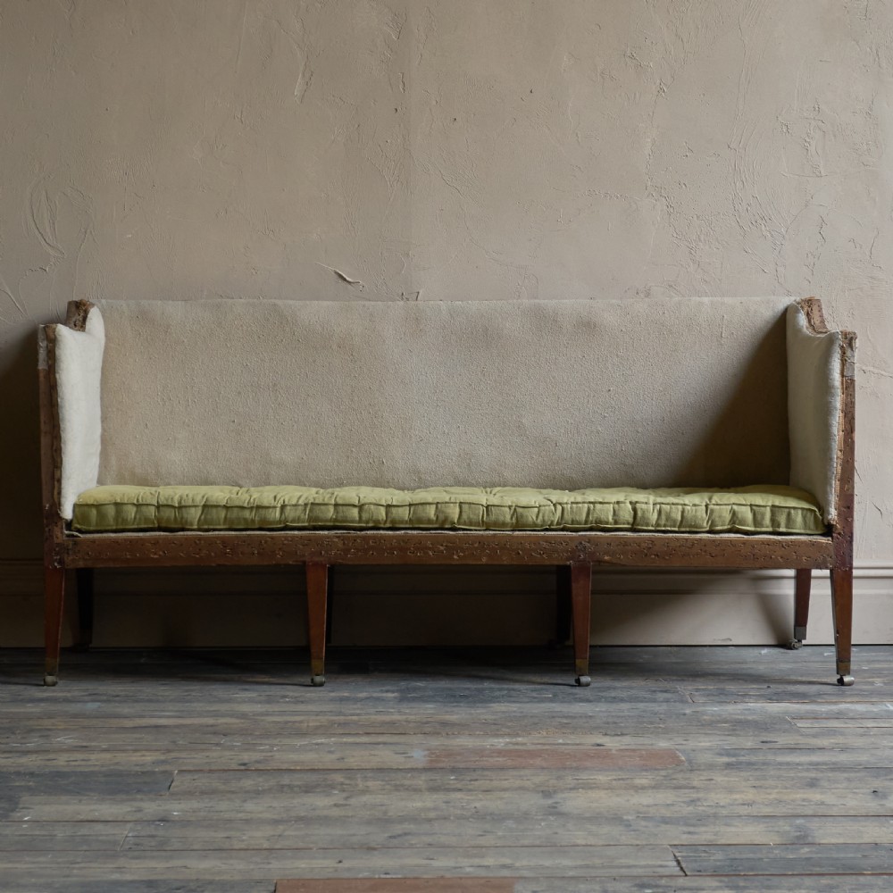 An antique Georgian square-back sofa featuring exposed wooden framing, eight legs with castors, and a yellow tufted seat cushion. View III