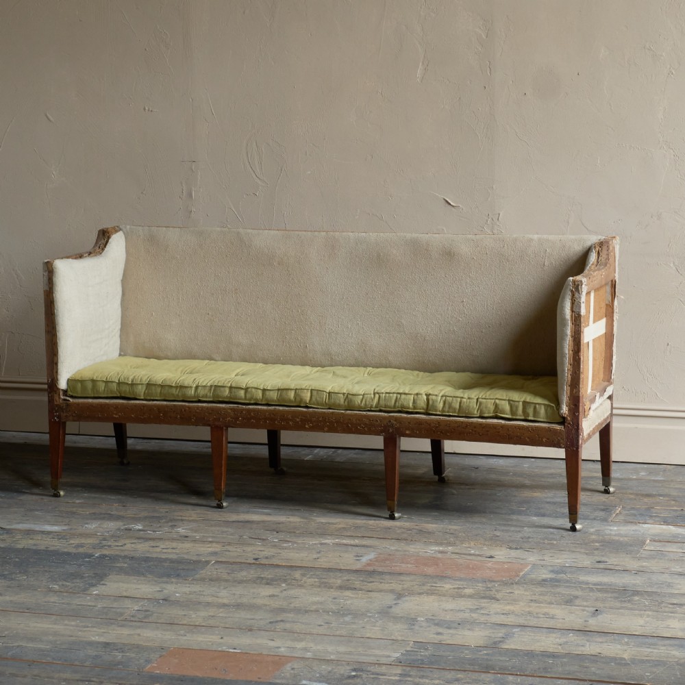 An antique Georgian square-back sofa featuring exposed wooden framing, eight legs with castors, and a yellow tufted seat cushion. View V