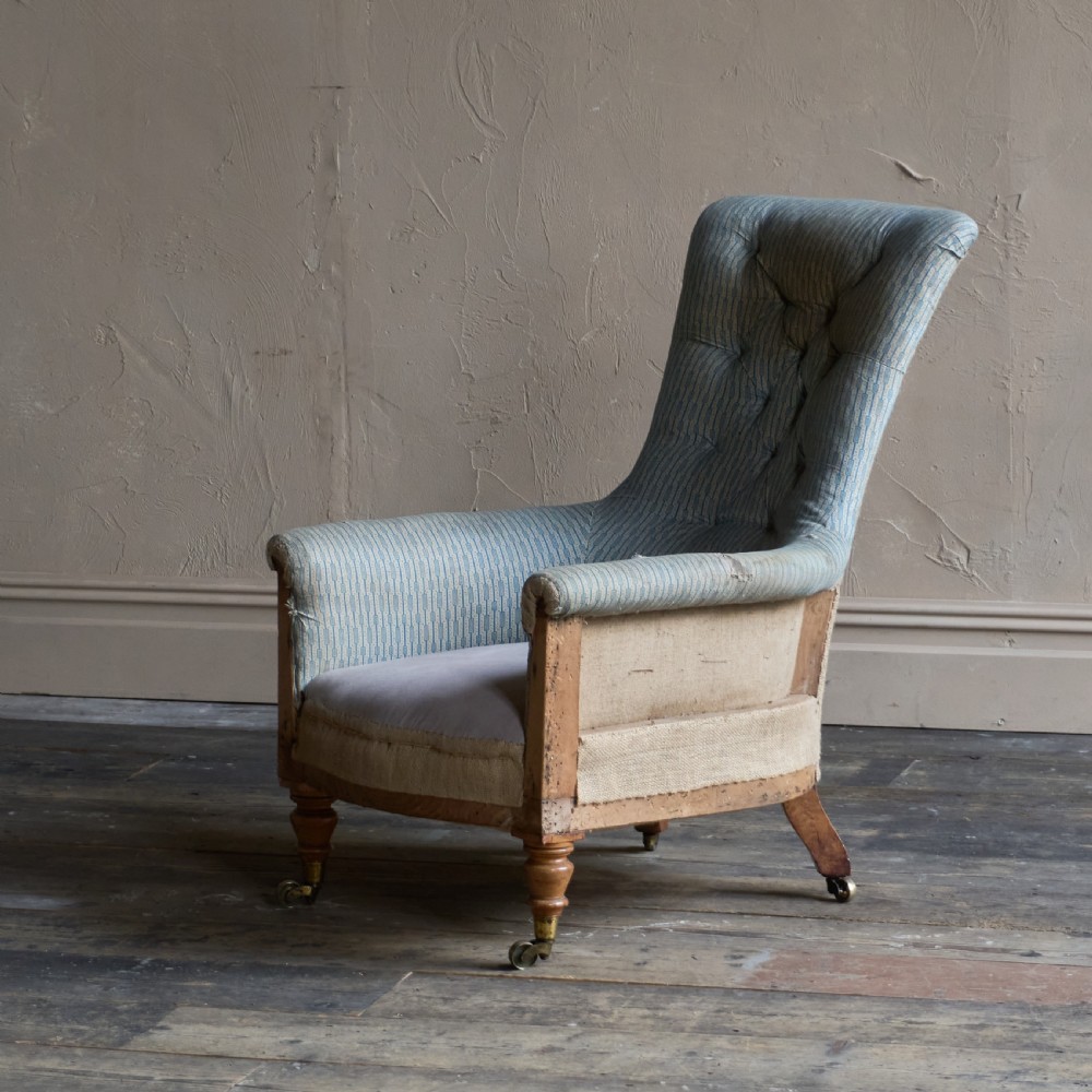 A Regency high-back library armchair featuring button-backed blue striped fabric, exposed hessian base, turned front wooden legs, and brass castors.