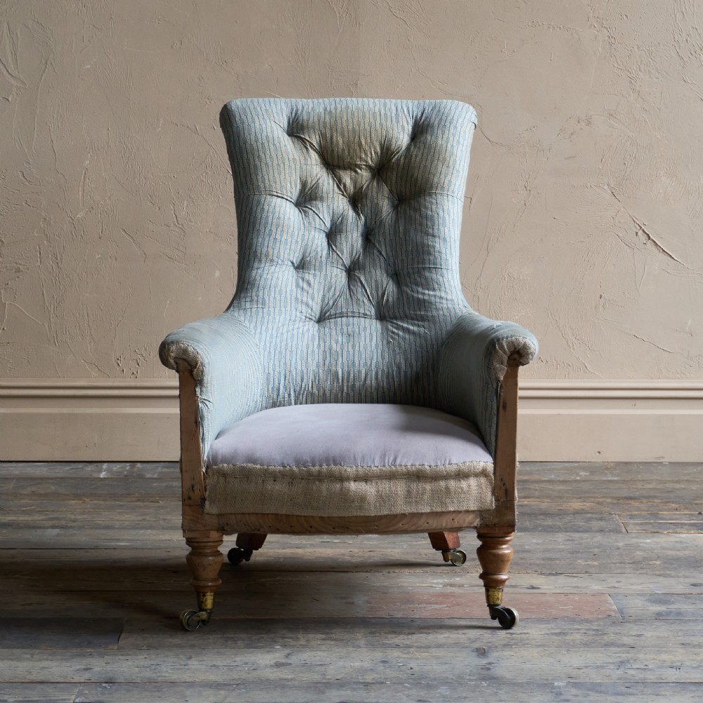 A Regency high-back library armchair featuring button-backed blue striped fabric, exposed hessian base, turned front wooden legs, and brass castors. View III