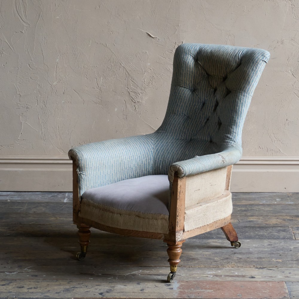 A Regency high-back library armchair featuring button-backed blue striped fabric, exposed hessian base, turned front wooden legs, and brass castors. View IV