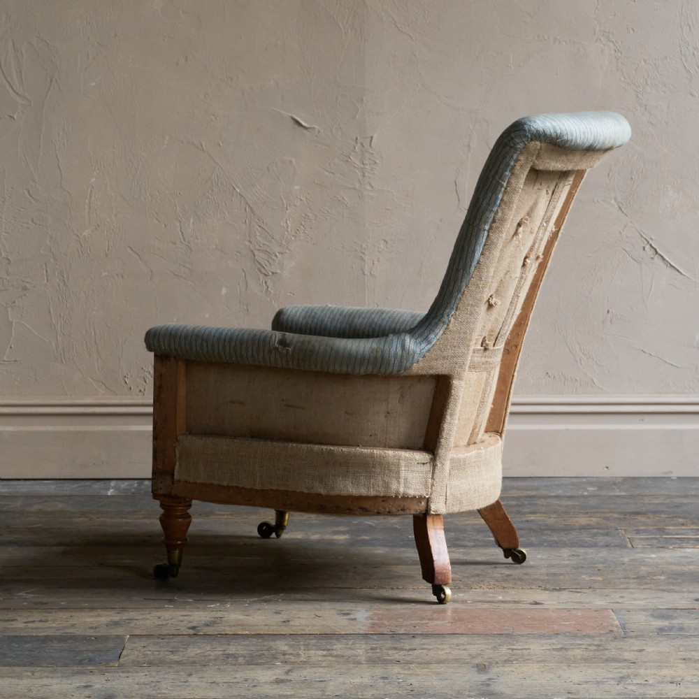 A Regency high-back library armchair featuring button-backed blue striped fabric, exposed hessian base, turned front wooden legs, and brass castors. View V