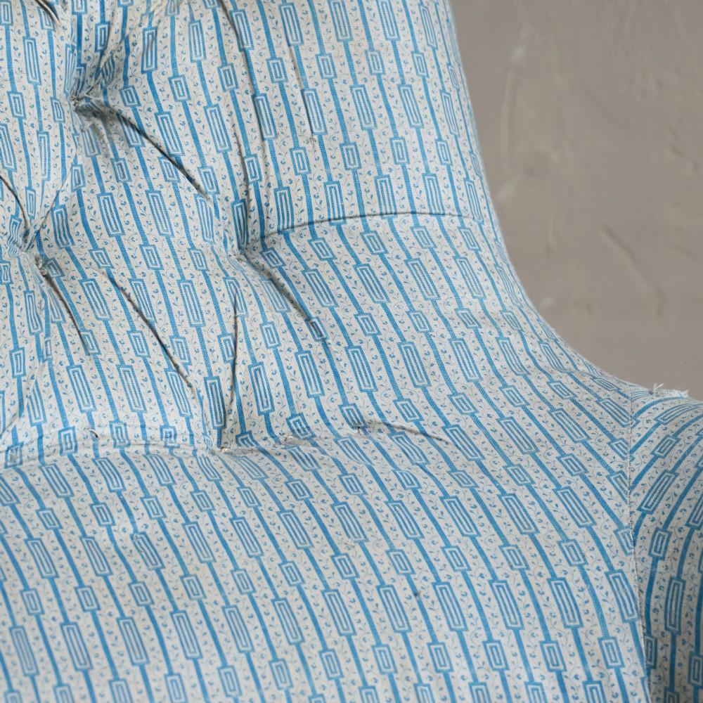 A Regency high-back library armchair featuring button-backed blue striped fabric, exposed hessian base, turned front wooden legs, and brass castors. View X