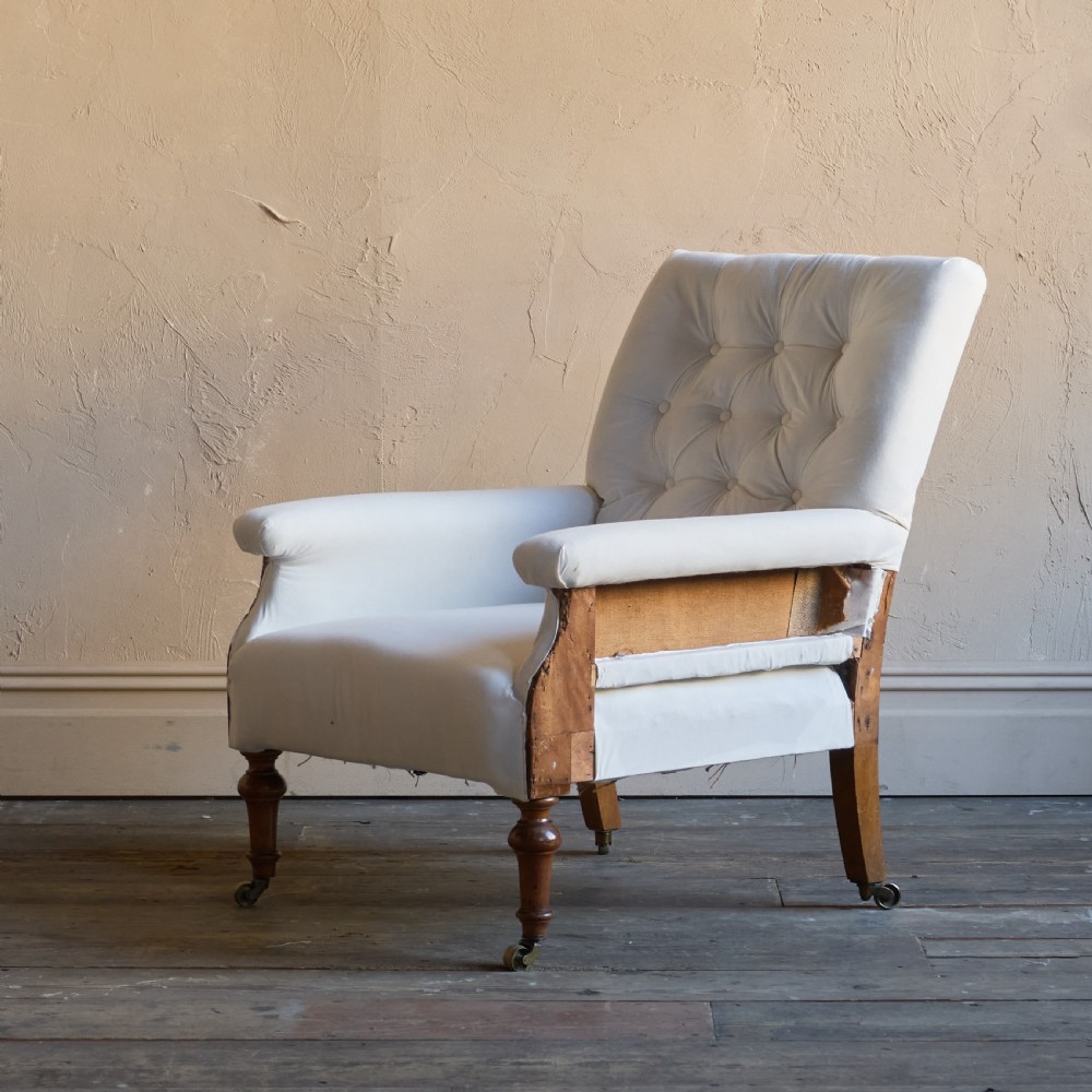An antique square back armchair upholstered in white calico fabric featuring deep buttoning and turned wooden legs with brass castors.