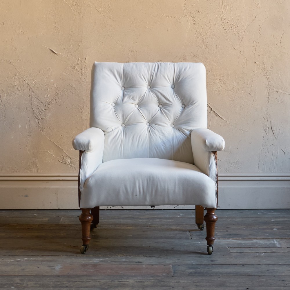 An antique square back armchair upholstered in white calico fabric featuring deep buttoning and turned wooden legs with brass castors. View II