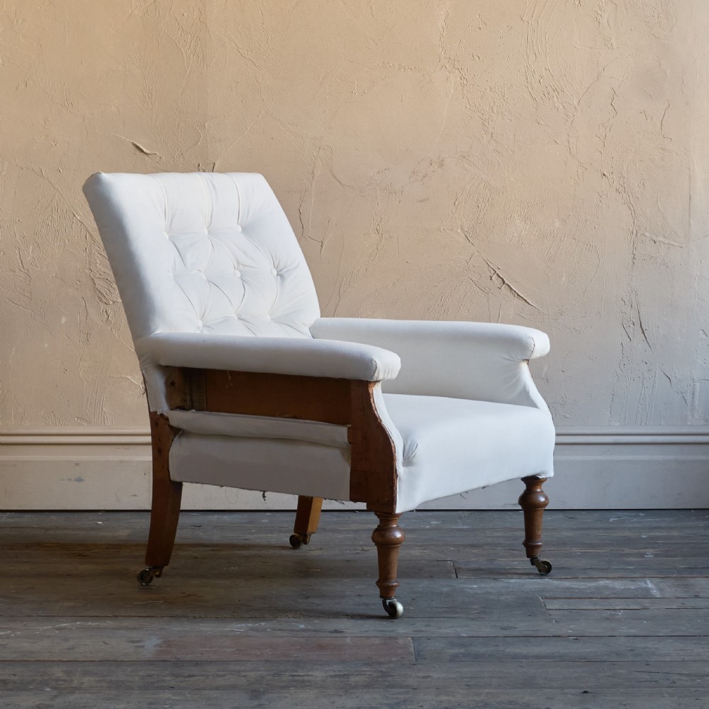 An antique square back armchair upholstered in white calico fabric featuring deep buttoning and turned wooden legs with brass castors. View III
