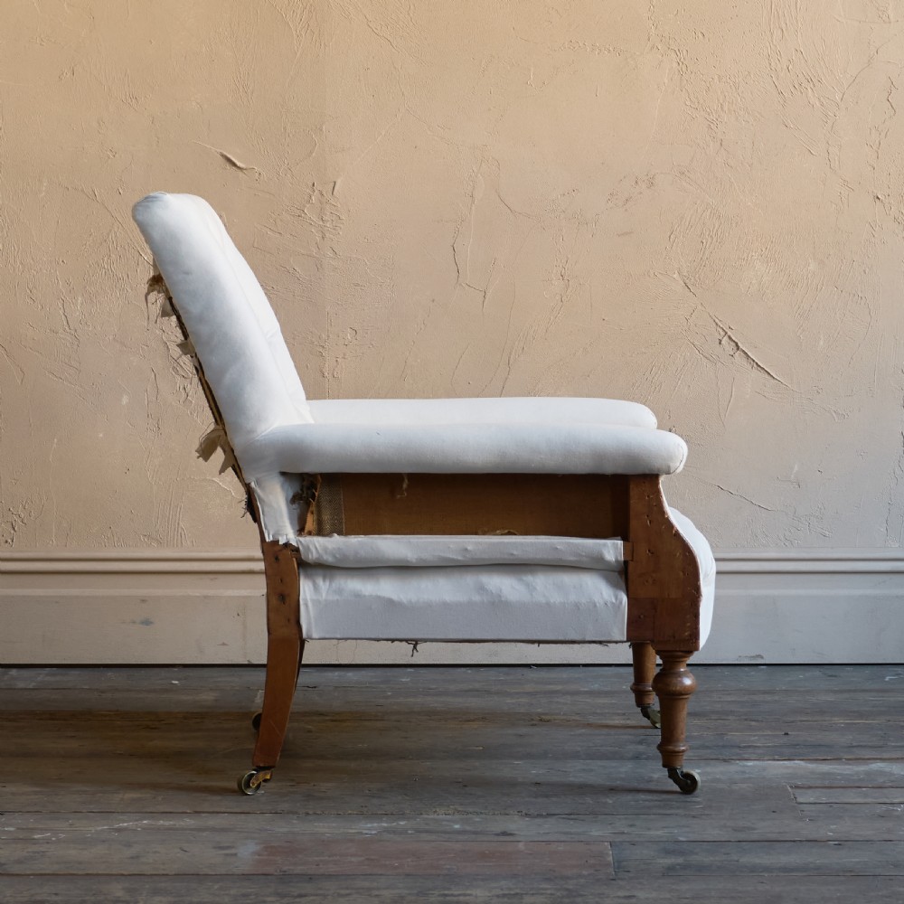 An antique square back armchair upholstered in white calico fabric featuring deep buttoning and turned wooden legs with brass castors. View V