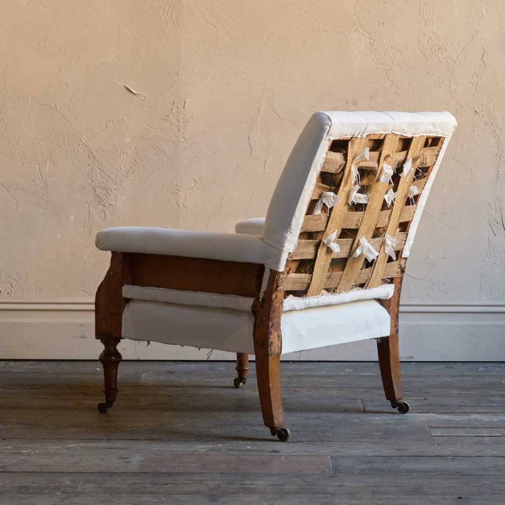 An antique square back armchair upholstered in white calico fabric featuring deep buttoning and turned wooden legs with brass castors. View VI