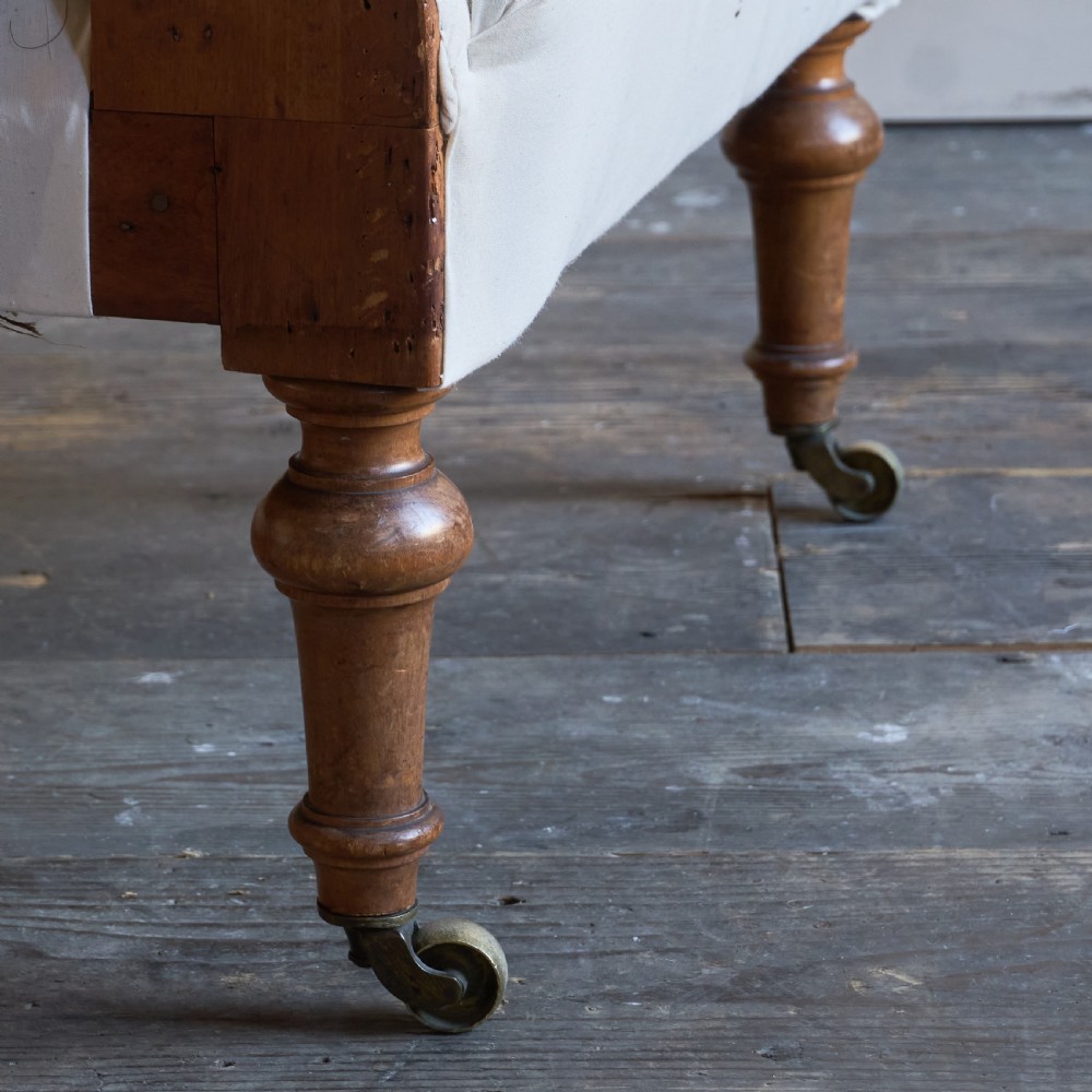 An antique square back armchair upholstered in white calico fabric featuring deep buttoning and turned wooden legs with brass castors. View VII