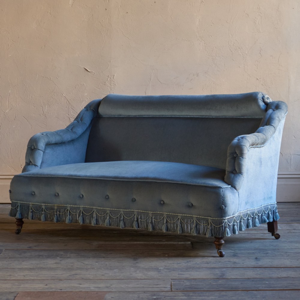 A Victorian bedroom settee upholstered in light blue velvet with buttoned details along the armrests and base, fitted with a tassel fringe skirt and turned wooden legs on castors. View III